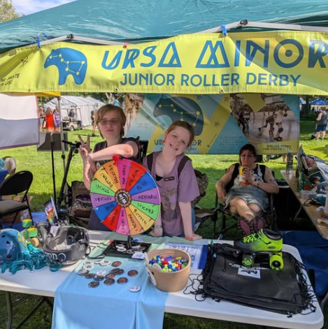 Two Ursa Minor skaters standing in the Ursa Minor booth at the 2026 TC Pride celebration